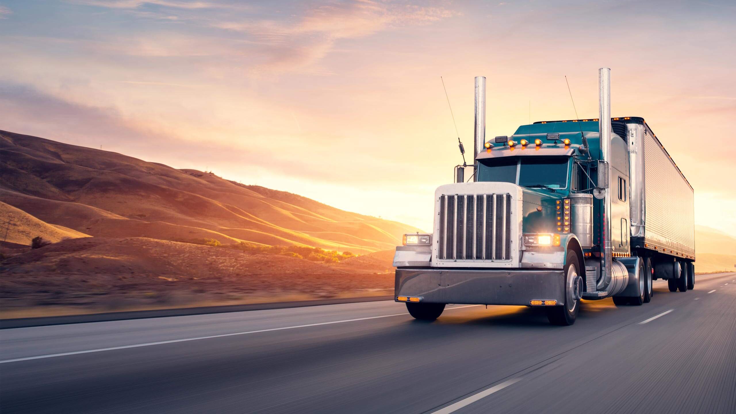Semi trucks rolling down an interstate highway at dusk
